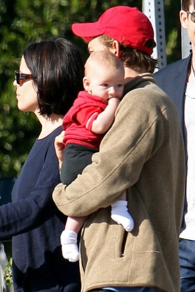 JJ Feild in a light brown jacket and red cap holding his baby with his wife in a blue tops.